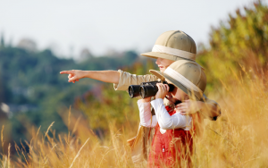 Children with binoculars and hats exploring around them 
